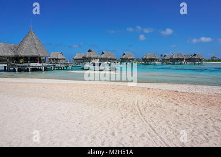 Tropical resort, beach sand with thatched bungalows over water in the lagoon, Tikehau atoll, Tuamotus, French Polynesia, Pacific ocean, Oceania Stock Photo