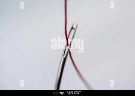 A red thread, threaded through the eye of a needle. Macro photography. Stock Photo
