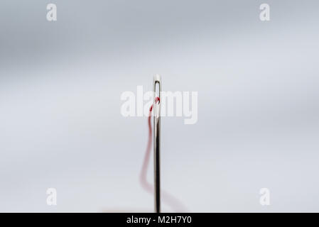 A red thread, threaded through the eye of a needle. Macro photography. Stock Photo