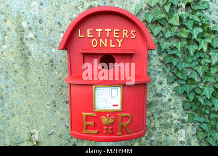 Novelty red bird box for nesting / breeding, hanging on a garden wall, resembling a British postbox, with Royal Mail Crown emblem, and 'letters only'. Stock Photo