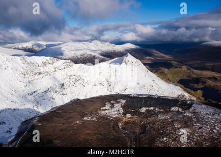 Icy trig point on Snowdon summit with view from top to Crib Goch beyond in winter snow in mountains of Snowdonia National Park. Wales, UK, Britain Stock Photo