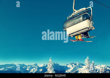 people in chairlift at ski resort above snowy trees and mountains Stock Photo