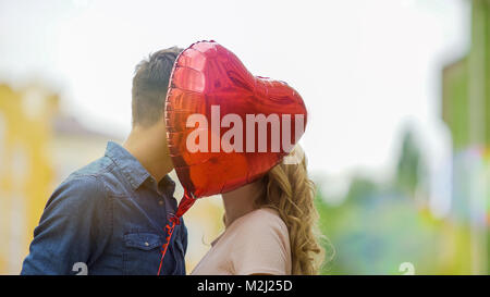 Happy couple kissing, hiding behind heart balloon, romantic relationship, date, stock video Stock Photo