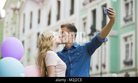 Sweethearts kissing in front of smartphone camera taking romantic selfie on date, stock video Stock Photo