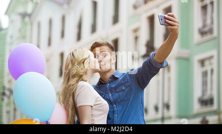 Guy taking selfie with attractive blonde girl kissing him, romantic date, love, stock video Stock Photo