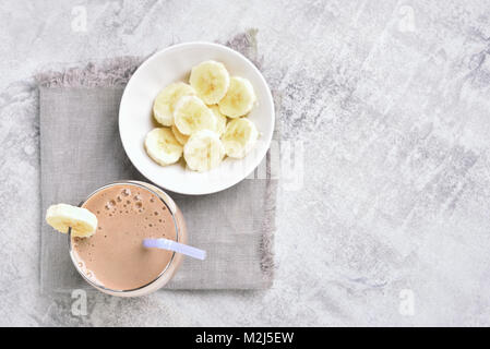 Homemade banana smoothie and banana slices on stone background with copy space. Healthy beverage. Top view, flat lay Stock Photo