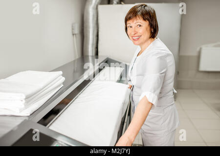 Laundress working with ironing machine Stock Photo