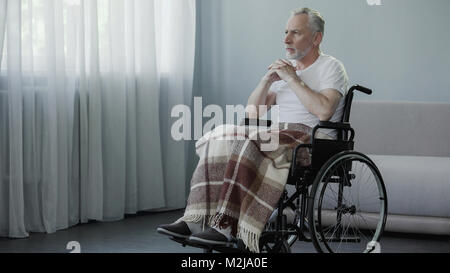 Senior disabled man sitting in wheelchair and looking in window, waiting family, stock footage Stock Photo