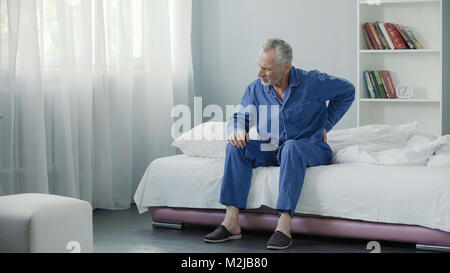 Senior male suffering sharp back pain, sick person getting up from bed, morning, stock footage Stock Photo