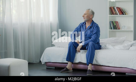 Pleased male in his 50s sitting on couch and smiling after morning gymnastics, stock footage Stock Photo