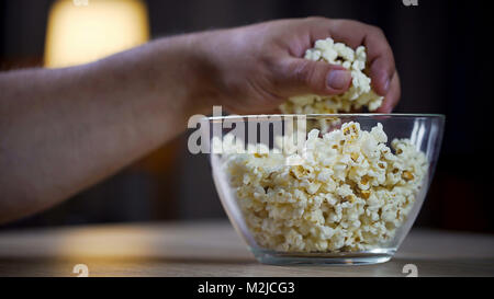 Closeup of male hand taking popcorn from bowl on table, unhealthy food addict, stock footage Stock Photo