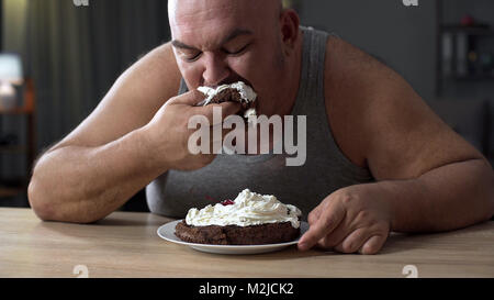 Messy obese man greedily eating cake with whipped cream, addiction to sweets, stock footage Stock Photo