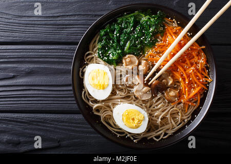 Asian Soba soup with vegetables, mushrooms, egg and sesame seeds close up in a bowl. horizontal top view from above Stock Photo