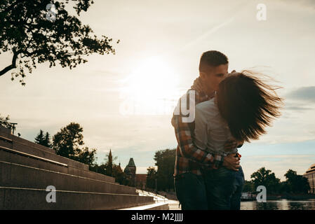 Emotional portrait of the beautiful loving couple hugging in the town street during the sunset. The girl is shaking her hair. Stock Photo