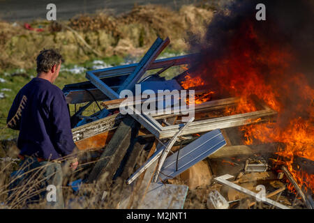 Person monitoring a burning fire of rubbish from a house renovation with flames and black smoke, probably with toxic fumes polluting the environment Stock Photo