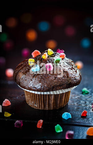 Funny Chocolate Muffin with candies on wooden table with bokeh background. Selective focus. Stock Photo