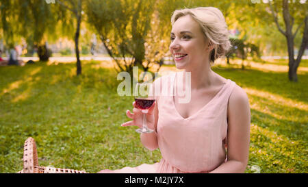 Pretty girl sipping wine in shade of park trees spending wonderful time in park Stock Photo