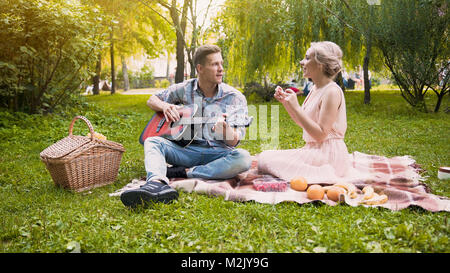 Couple having romantic date, singing songs and playing guitar, sitting in park Stock Photo