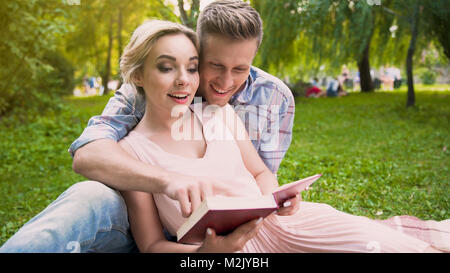 Couple of students in love sitting on rug reading educational book together Stock Photo