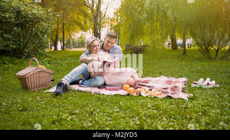 Couple of lovers reading novel book sitting on rug during picnic, romantic date Stock Photo