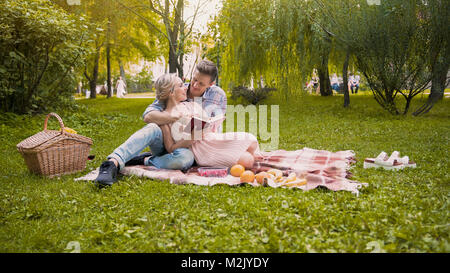 Loving couple discussing book, sitting on rug during picnic, romantic date Stock Photo