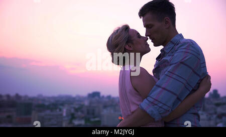 Handsome guy tenderly embracing his beautiful lady on open terrace, cityscape Stock Photo
