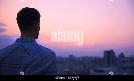 Young man standing on roof of building alone and meditating, enjoying freedom Stock Photo