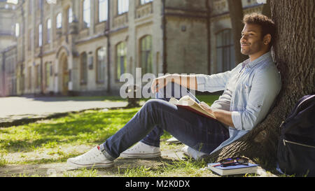 Multiracial guy sitting under tree, looking and smiling at somebody, friendly Stock Photo