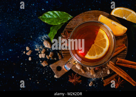 Dark still life with a teacup, lemon slices, anise stars, sugar, tea leaves and cinnamon on a dark background. Autumn tea cup from above. Copy space. Stock Photo