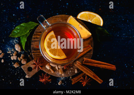 Dark still life with a teacup, lemon slices, anise stars, sugar, tea leaves and cinnamon on a dark background. Autumn tea cup from above. Copy space. Stock Photo