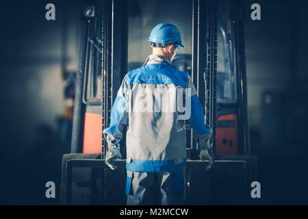 Caucasian Warehouse Forklift Operator in Front of His Lift Truck. Moving and Lifting Equipment. Stock Photo