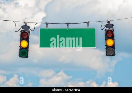 Horizontal shot of two yellow traffic lights hanging from a cable with a blank street sign in-between with blue sky and clouds behind it. Stock Photo