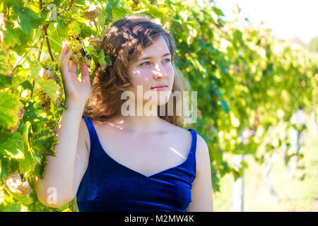 Closeup portrait of elegant young woman's face by vineyard winery grapevine leaves green in Virginia holding grapes, touching with hands Stock Photo