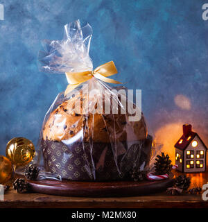 Italian festive bread panetton with a transparent wrapper on a table decorated for Christmas. and two glasses of champagne. New Year's traditional des Stock Photo