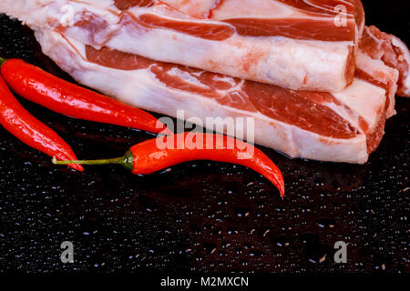 Raw lamb shanks with pepper on stone tray on black table, selective focus Stock Photo