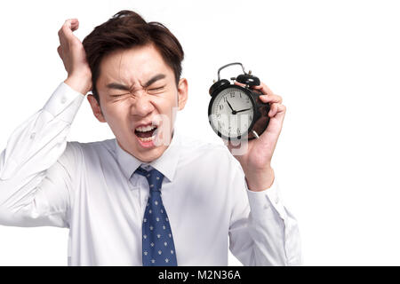 A young business man with an expression of pain holding the alarm clock Stock Photo