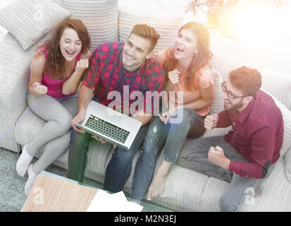 triumphant group of friends laughing while sitting on the couch in the living room Stock Photo