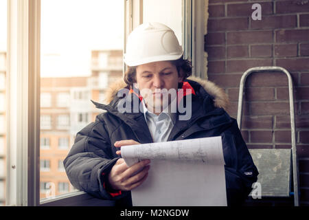 Engineer-builder working with documents on the construction site. Worker inspects drawings on the construction site against the background of brick wa Stock Photo