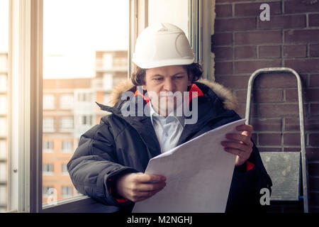 Engineer-builder working with documents on the construction site. Worker inspects drawings on the construction site against the background of brick wa Stock Photo