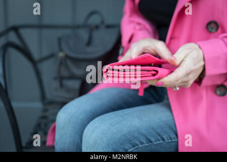 woman sitting on bench wearing coordinating pink coat, wallet and nail polish Stock Photo