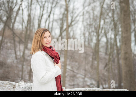 pretty woman standing in snowy forest with light snow falling and blowing Stock Photo