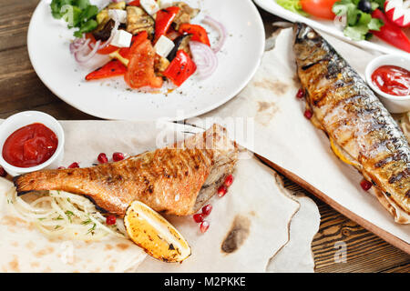 grilled mackerel and sea bass. Salad of fresh vegetables. Serving on a wooden Board on a rustic table. Barbecue restaurant menu, a series of photos of different meats anf fish Stock Photo