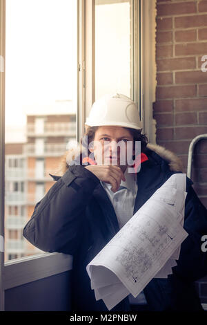 Pensive young man builder in hard hat standng and thinking. Soft focus, toned Stock Photo