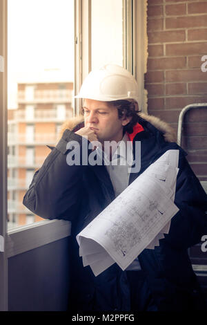 Pensive young man builder in hard hat standng and thinking. Soft focus, toned Stock Photo