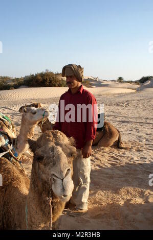 A Berber guide and camels resting in the desert sand near Douz, Tunisia Stock Photo