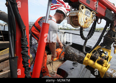 Deckhand James Jarrell cuts a large piece of debris removed from the Elizabeth River that will not fit on the deck of the Corps Vessel Harrell days after Hurricane Irene came through the area.   The Hampton Roads Harbor Debris Removal Project, which takes place all year long, ensures the federal navigation channel is safe for commercial shipping and boaters.  (U.S. Army Photo/Patrick Bloodgood) 110830-A-OI229-027 by norfolkdistrict Stock Photo