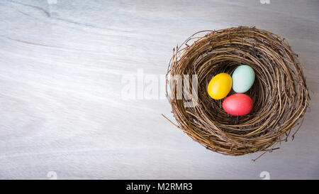 Flat Lay with copy space of  colorful Easter eggs in a rustic nest or basket on wooden background. Natural light. Selective Focus. Stock Photo