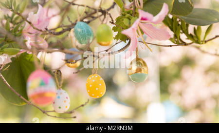 Pretty decorated colored Easter eggs with modern patterns hanging on a tree branch with lovely pink flower blossoms on a sunny spring day. Selective f Stock Photo