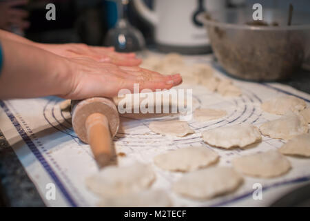 Close up of woman hands holding rolling pin and preparing traditional polish christmas dish called pierogi, dumplings filled with mushroom and onion f Stock Photo