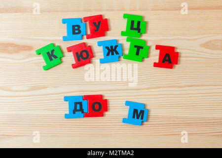On a wooden background lie the letters of the Russian alphabet. The child laid out the inscription of the house in Russian Stock Photo